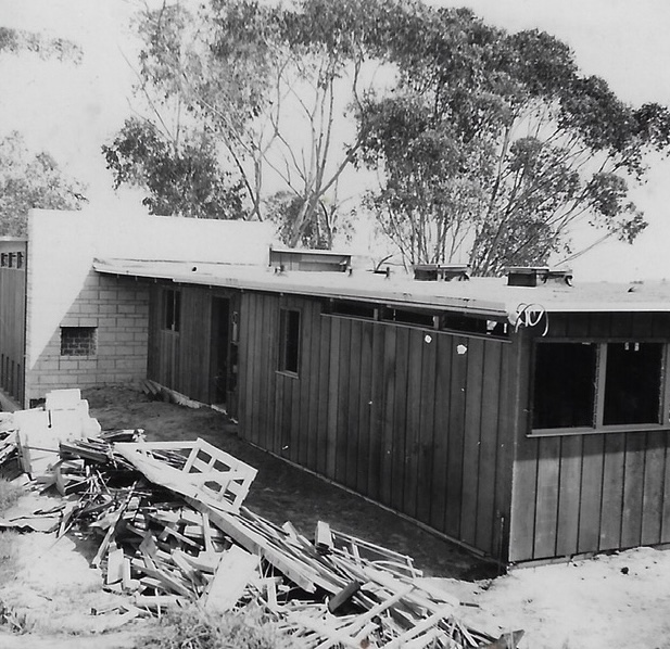 Redwood exterior with lumber pile, March 1955
